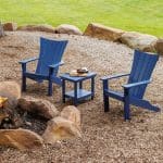 a set of 2 dark blue Wavz Adirondack chairs with a matching end table sitting in front of a firepit.