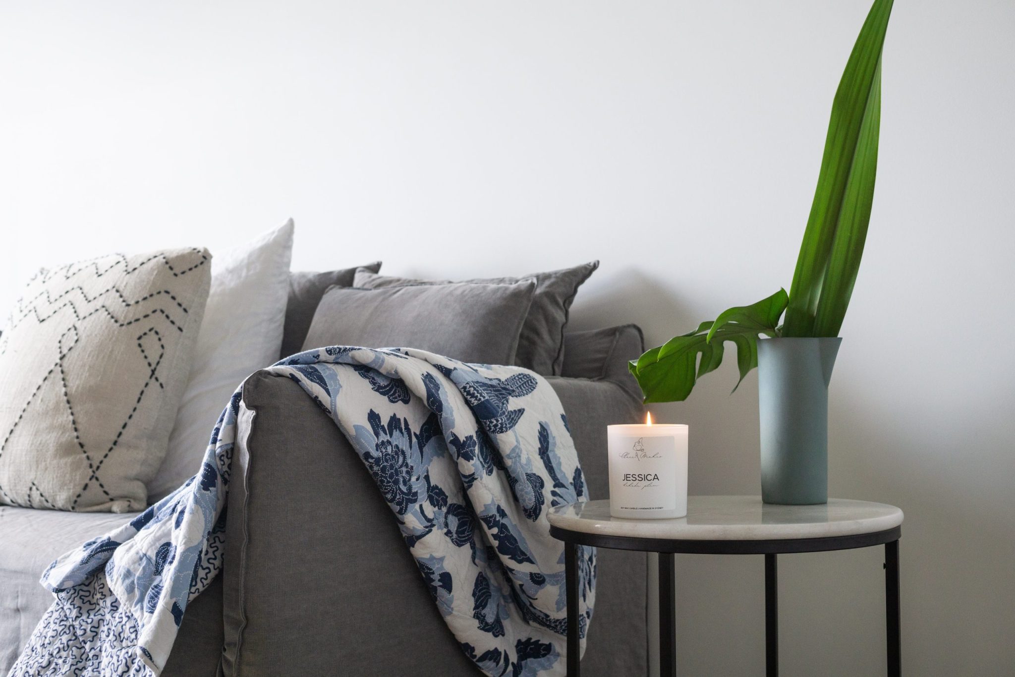 Couch with throw pillows, throw blanket, side table, lit candle, and plant.