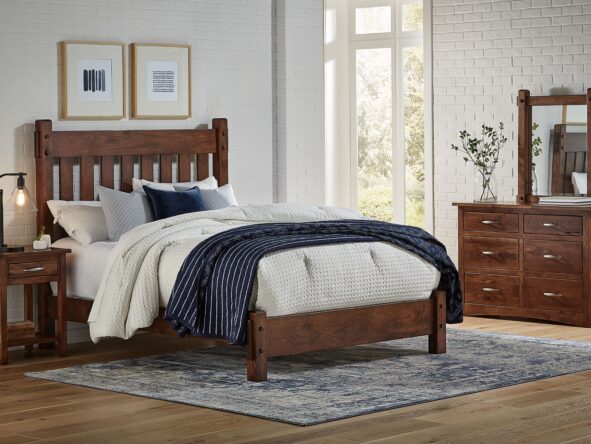 Bedroom with dark brown hardwood bed, nightstand, and dresser in a room with white walls, a blue and white rug, and tan wood plank flooring.