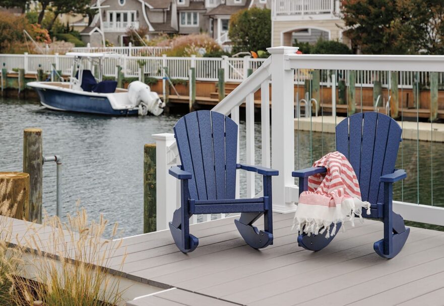 Set of 2 navy blue poly lumber rocking chairs on a deck by a boat marina.