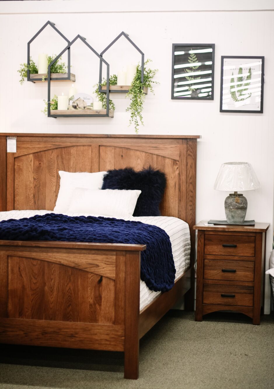 Brown wood bed with white and blue bedding and matching nightstand in a room with tan carpet, white walls, and plant decor.