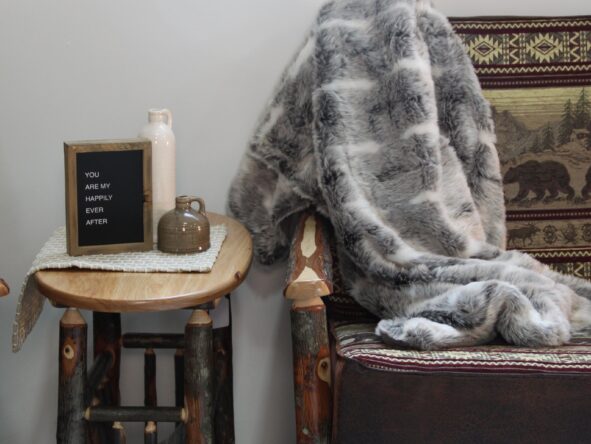 Rustic log trim sofa and end table with a gray and white throw blanket, 2 ceramic vases, and a small wood letterboard.