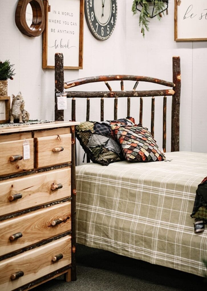Rustic log bedroom set on display with a dresser and bed that has a light colored plaid comforter and multi-colored quilt pillows.