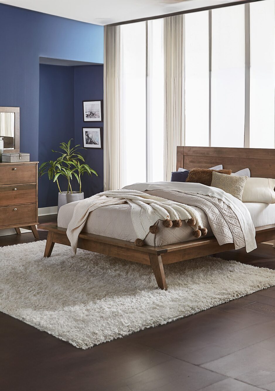 Liberty Bed and bedroom set with brown stained hardwood bed, dresser, and nightstand in a room with hardwood flooring, a large white rug, and a dark blue accent wall.