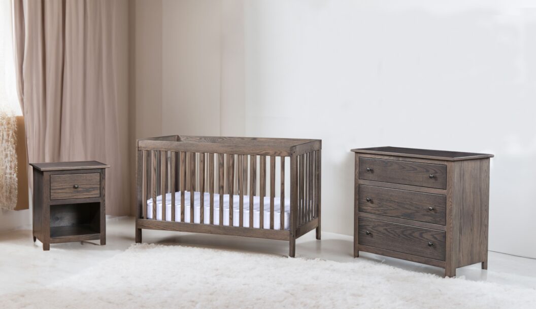 Brown hardwood crib, dresser, and nightstand in a nursery with white walls, a large white rug, and blush pink curtains.