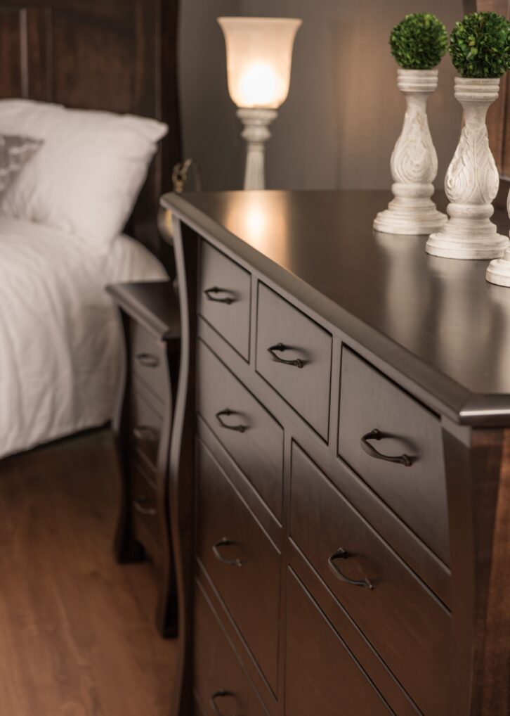 Close up of a dark brown hardwood dresser with a matching nightstand and bed in the background.